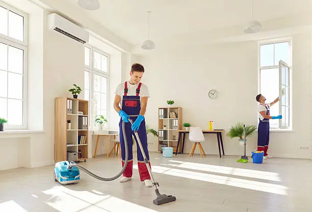 Two professional cleaners from The Kleeners performing deep apartment cleaning in a bright Dubai living room using advanced vacuum equipment and window cleaning tools.